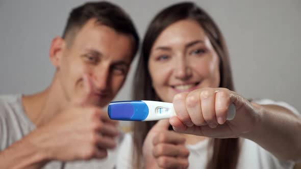 Closeup of Positive Pregnancy Test on Blurred Background of Happy Man and Woman Slow Motion