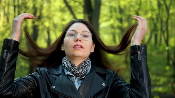 Attractive Young Brunette Woman in Glasses Straightens Her Hair in the Forest