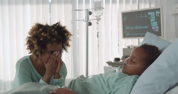 Upset Young African Woman Crying Sitting Near Little Daughter Sleeping in Bed at Hospital