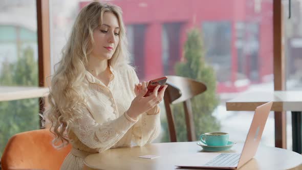 Elegant Slim Beautiful Woman Sitting in Cafe Surfing Internet on Smartphone