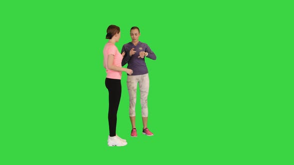 Two Beautiful Girls in Sportswear Setting Up the Fitness Smart Watch for Running on a Green Screen