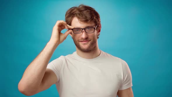 Young Man Taking Off His Glasses Slowly Against Blue Background