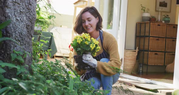 Smiling caucasian woman planting yellow flowers in sunny garden her pet dog watching her