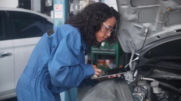 Young woman is mechanic holding tablet computer checking engine of car in the garage.
