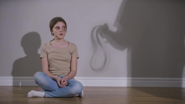 Scared Girl Looking Away Hugging Self As Parent Shadow Frightening Teenager with Belt