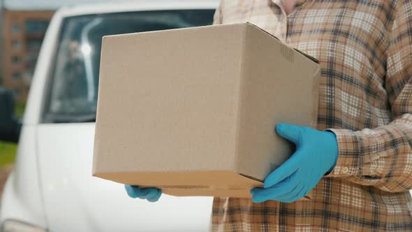 A Delivery Service Worker Holds a Parcel Stands Near a Van