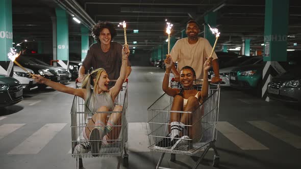 Group of Happy Diverse Friends Riding on Shopping Carts at Underground Parking Ladies Holding