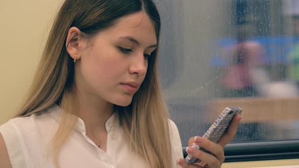 Portrait Of Young Caucasian Woman Riding In A Subway Car And Using A Smartphone