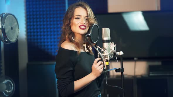 Beautiful singer with pretty smile standing at the microphone on the studio background.