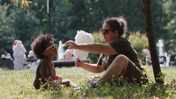 Mixed Family of Mother and Daughter in Sunglasses Spending Time in the Park Eating Cotton Candy