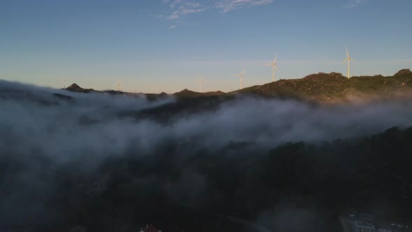 Wind turbines spinning on top of hills at sunrise and clouds carpet, Caramulo in Portugal. Aerial fo