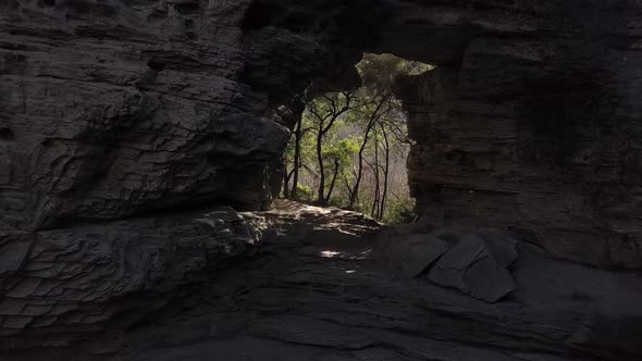 Natural arch formed in huge rock with glimpse of forest full of light