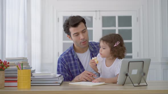 Father and little cute daughter watching the video tutorial on the tablet and teaching homework 