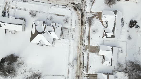 Top down aerial view over residential neighborhood after a snowstorm with plowed street.
