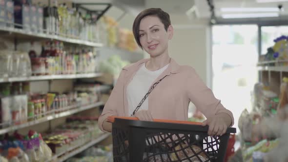 Portrait of Smiling Young Caucasian Woman Posing with Shopping Basket in Grocery, Beautiful Brunette