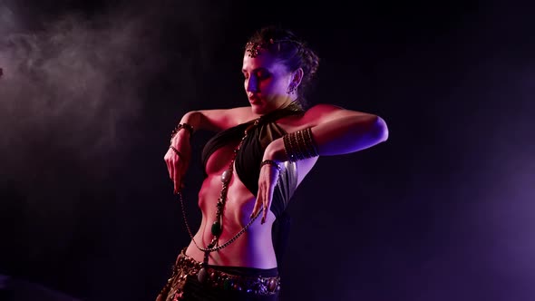 A Woman Dances an Oriental Dance on a Dark Smoky Background Holding a Chain in Her Hands