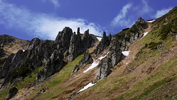 Rocky Cliff and Peak of Mountain with Steep Slope and Moss Against Cloudy Sky