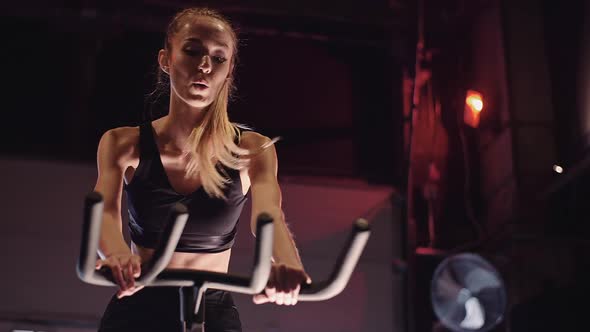 Young Fit Sporty Blone Girl Exercising on a Bike at Gym