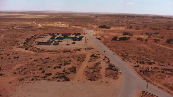 aerial static shot of army camp of tents in the middle of the endless desert next to an empty road w