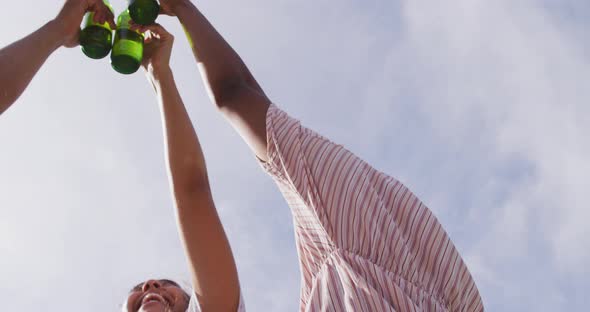 Hands of diverse friends making toast with bottles of beer in the sun at outdoor party