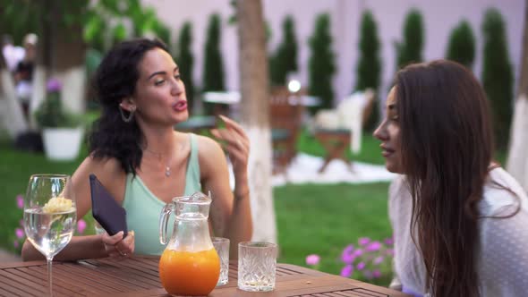 Two Excited Young Women Came to Sit at the Table at Outdoors Cafe Chatting Emotionally