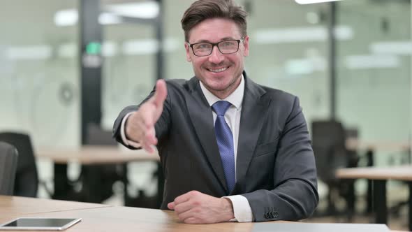 Middle Aged Businessman Showing Hand Shake Sign at Camera 