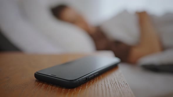 Woman Reaches Out to Turn Off Phone at Bedside Table