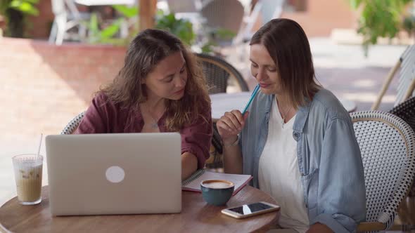 Happy Female Friends Working Together with Laptop at Outdoor Cafe