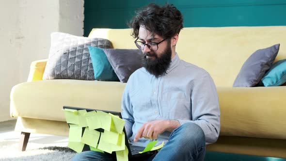 Man Working at the Computer with a Lot of Reminder Notes Sitting Near Sofa