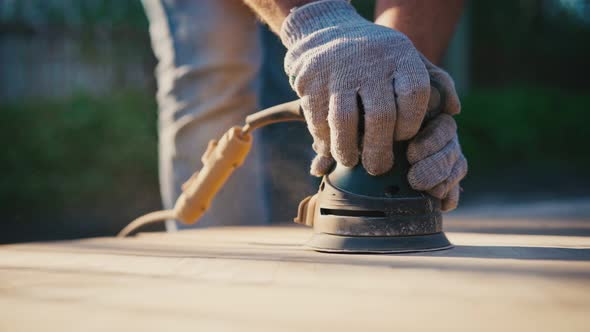 Man's Hands Grinds a Parquet Board with an Orbital Sander Outdoors