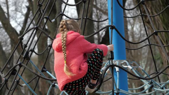 Schoolgirl Climbs Up Large Rope Net on Blue Metal Supports