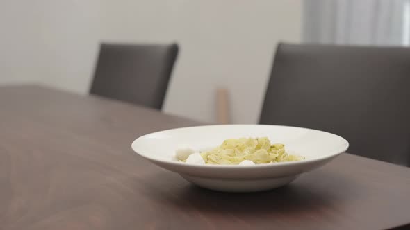 Slow Motion Man Add Mozzarella To Pesto Fettuccine in White Pasta Plate on Walnut Table