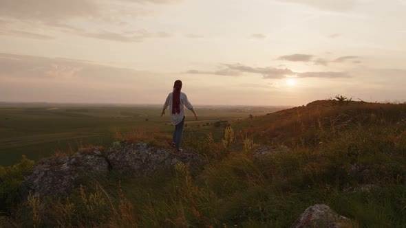 Girl Looks on the Sunset and Raises Hands Up