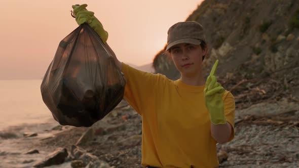 Volunteer picks up a polyethylene bag full of garbage, and shows a prohibition with her finger