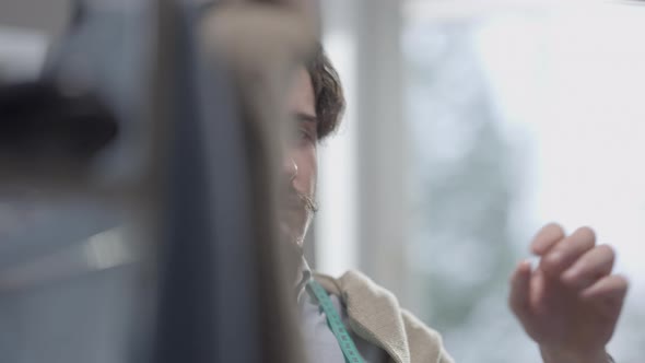 Closeup of Positive Skilled Caucasian Male Dressmaker Looking Through Clothes on Hangers Looking at