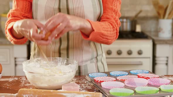 Woman wearing apron breaking an egg into the mixture in the kitchen 4K 4k