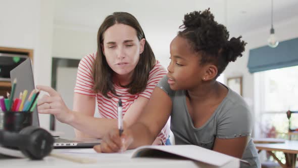 Happy caucasian woman and her african american daughter doing homework together