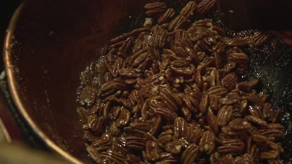 Close up slow motion shot of roasted caramelised pecan nuts being stirred with a big wooden paddle.