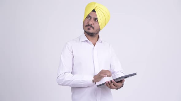 Happy Bearded Indian Sikh Businessman Thinking While Using Digital Tablet