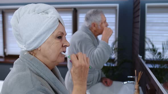 Senior Couple Man and Woman Brushing Teeth and Looking Into a Mirror at Luxury Bathroom at Home