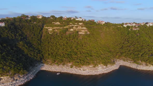 High slow pan of the cliffs on Lake Travis. Estates, Businesses, and Green trees can be seen on the