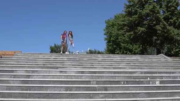 Two Beautiful Girls Girlfriends are Happy and Jumping Standing on the Steps on the Street