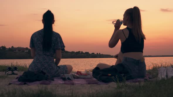 Two Friends on Picnic Women on Beach at Evening Eating and Talking