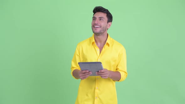 Happy Young Hispanic Businessman Thinking While Using Digital Tablet