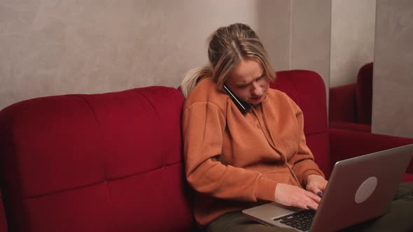 Busy Caucasian Woman Sitting on Couch in Living Room Talking on Mobile Phone and Working on Laptop