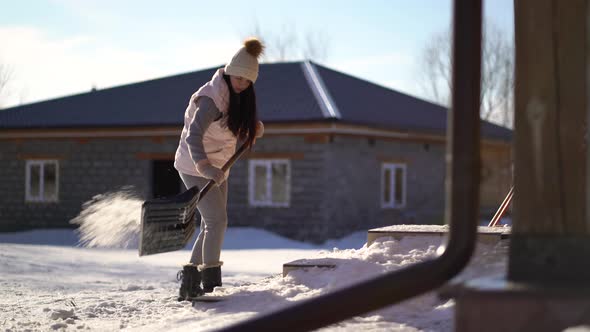 Woman Shoveling Snow on Backyard Near the House .