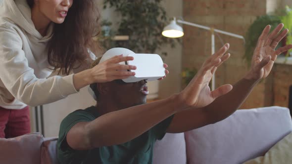 Joyous Black Man Using VR Glasses with Help of Wife at Home