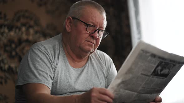 A Mature Man in Glasses Reading a Newspaper at Home