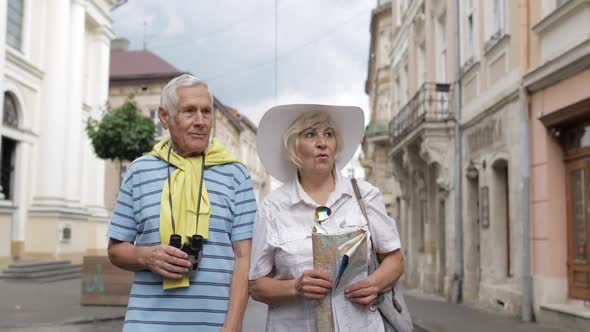 Senior Male and Female Tourists Walking with a Map in Hands Looking for Route