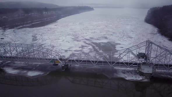 Drone flying high over swing bridge with big ice chunks on a snowy river in Connecticut during a win